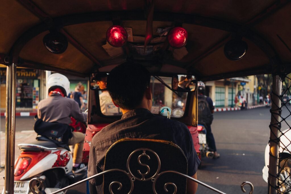 View from a tuk-tuk in Bangkok amidst motorcycle traffic at sunset.