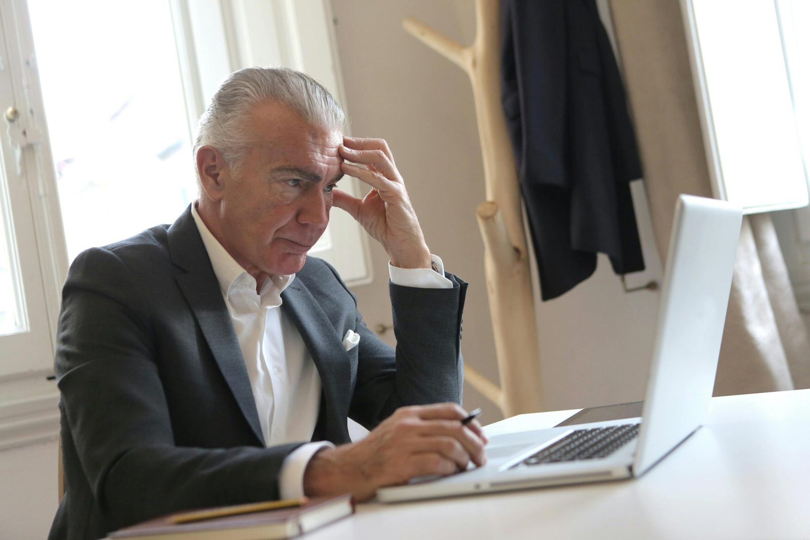 Senior businessman in office pondering work issues on laptop, showing stress.